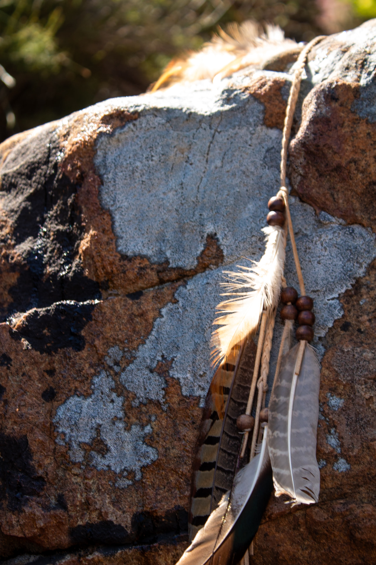 Feathers and beads resting against a sunlit lichen-covered boulder