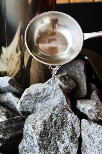 A ladle pouring water across the hot rocks of a sauna heater
